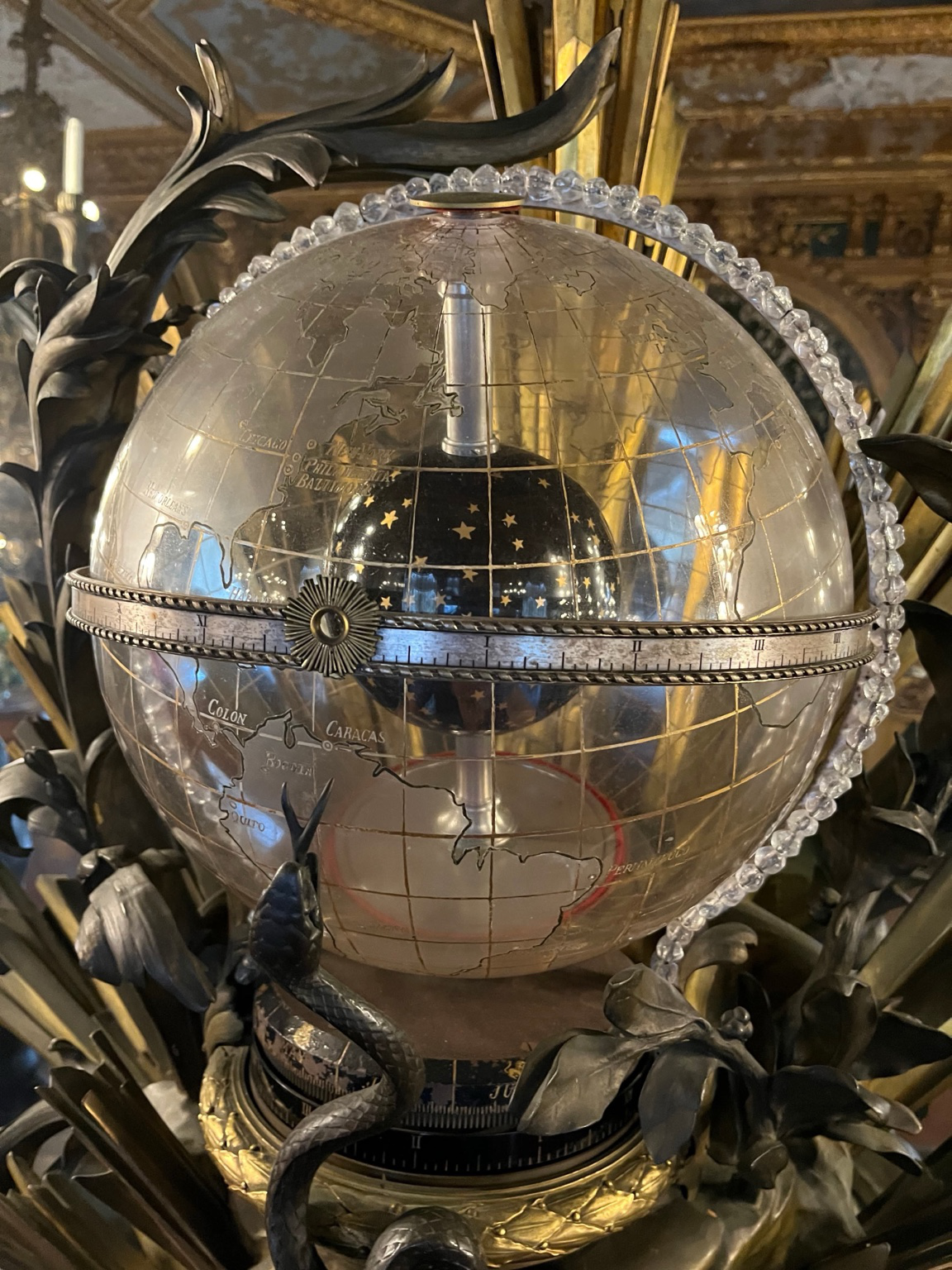 Frontal view of the globe-clock: transparent terrestrial shell, inner star sphere, equatorial band, and surrounding bronze ornament